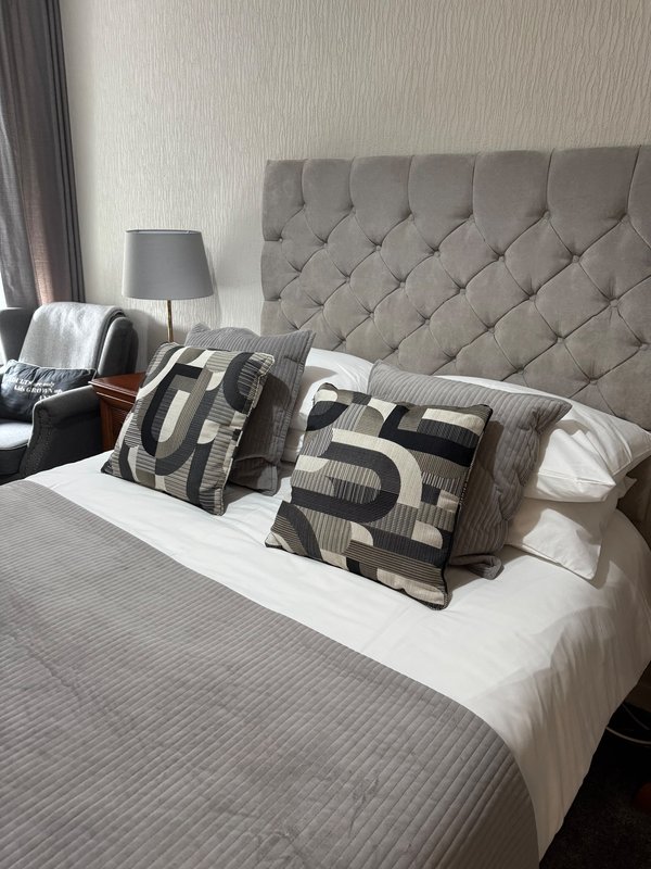 Modern bedroom with grey upholstered headboard, double bed, patterned cushions and bedside lamp