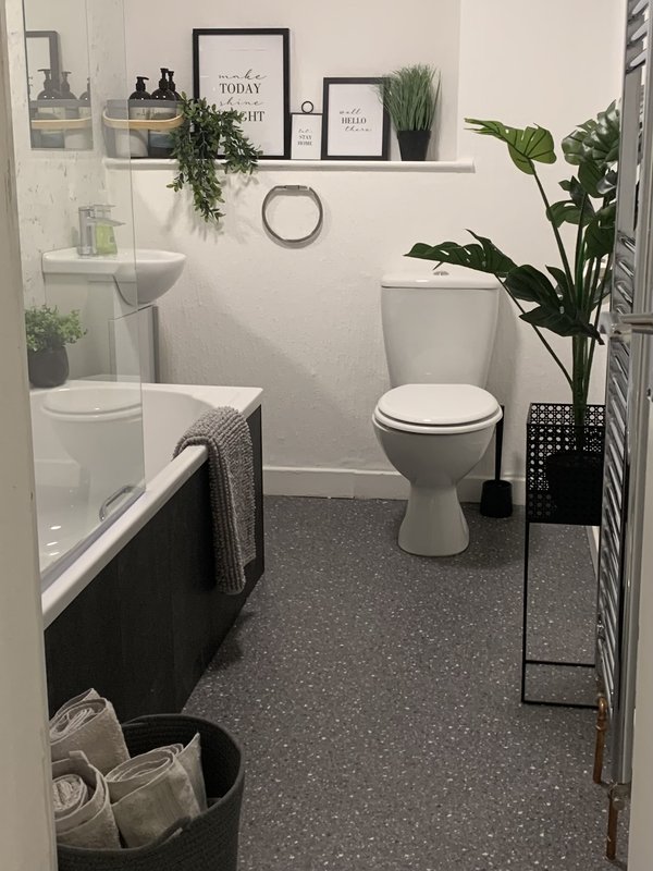 Modern bathroom with toilet, pedestal sink, bathtub, shelving with plants and decor