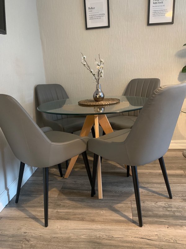 Modern dining area with round glass table, grey upholstered chairs and wooden floor