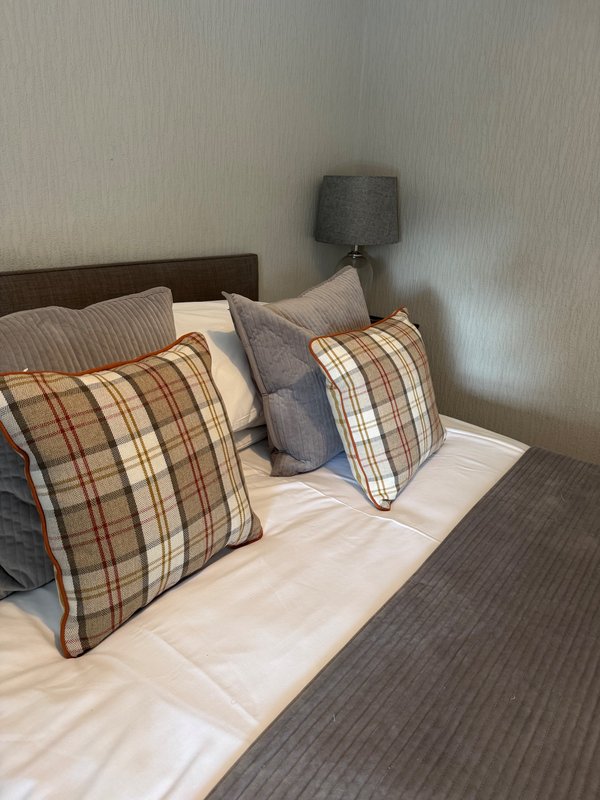 Bedroom with double bed, plaid cushions, white bedding and dark headboard