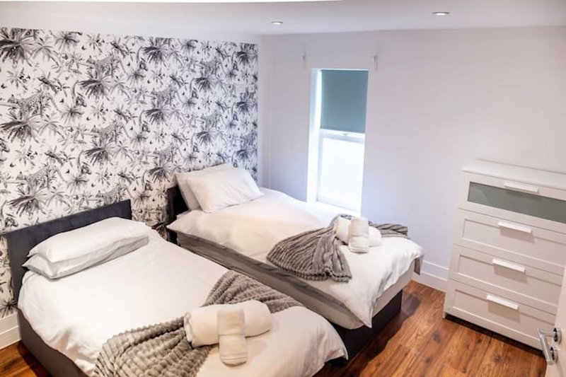 Twin bedroom with black bed frames, patterned wallpaper, white dresser and wooden flooring