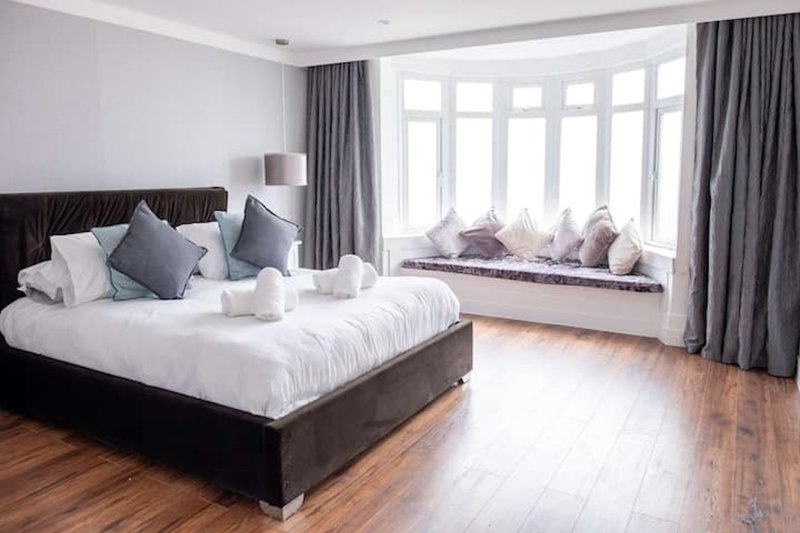 Spacious bedroom with dark bed, white bedding, gray cushions and window seat with pillows