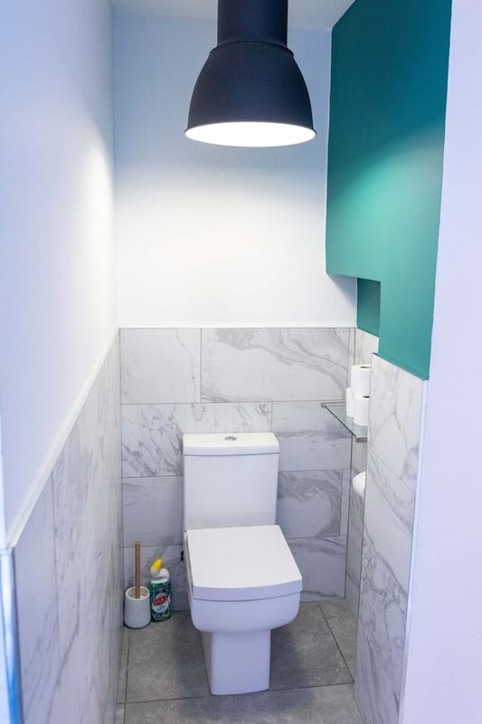Small bathroom with white toilet, marble wall tiles, pendant lamp and teal accent panel