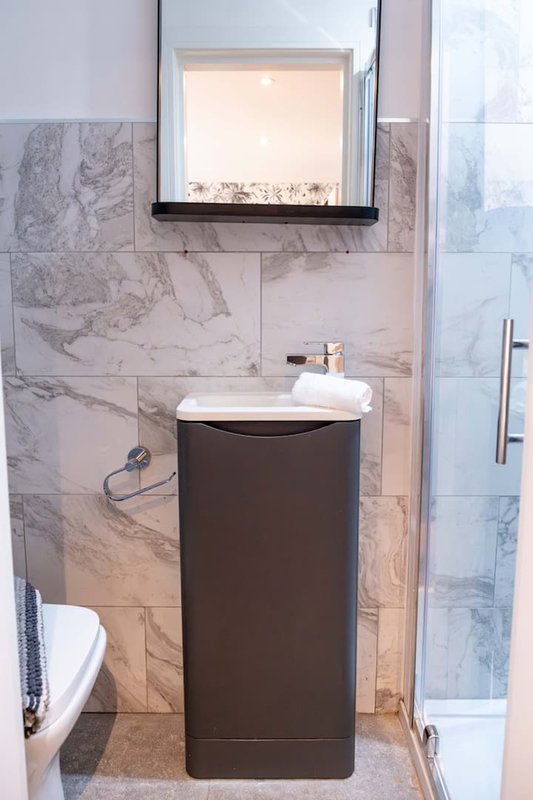Modern bathroom with marble tile walls, dark vanity cabinet, wall-mounted mirror and sink