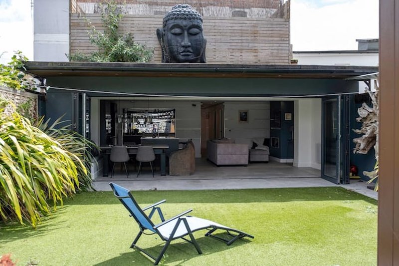 Modern outdoor patio with lounge chair, manicured lawn, and large Buddha sculpture