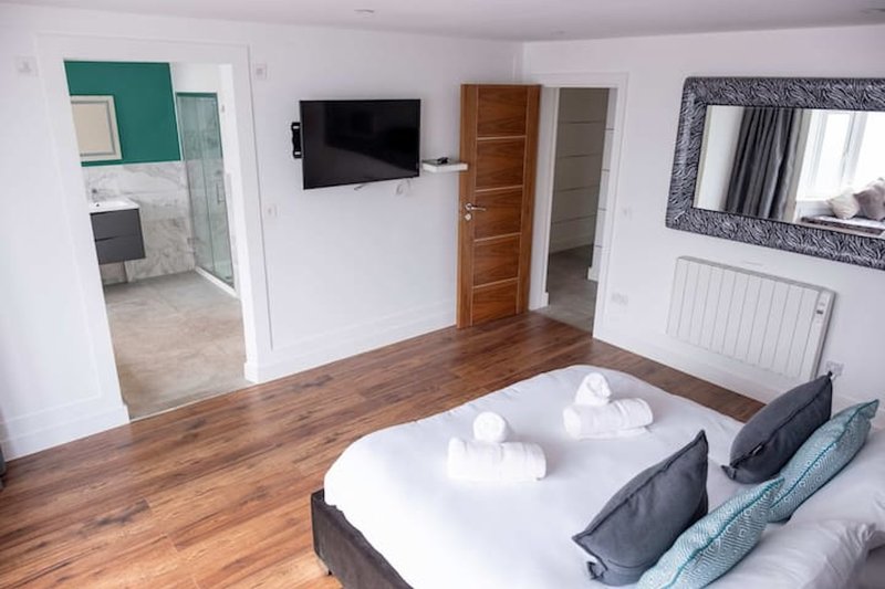 Spacious bedroom with double bed, wooden floor, wall-mounted TV, and ensuite bathroom access