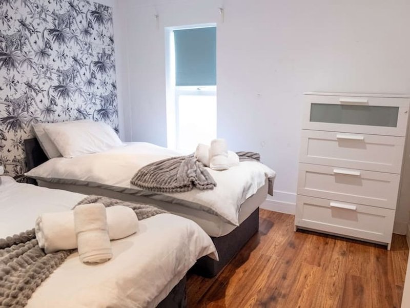Bright bedroom with two single beds, white bedding, wooden floor and chest of drawers