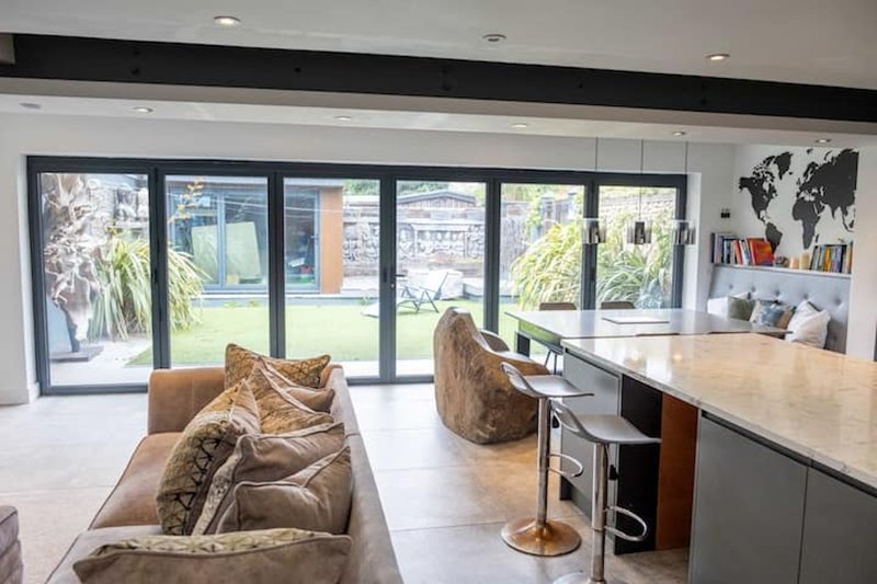 Open-plan living area with tan sofa, kitchen island, and large glass doors opening to garden