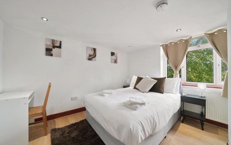 Bright bedroom with double bed, wooden flooring, large window with curtains and garden view