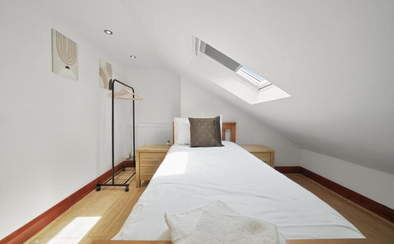 Attic bedroom with single bed, wooden floor, skylight and minimal furnishings