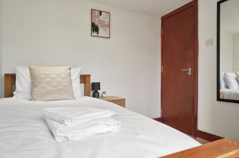 Modern bedroom with double bed, white bedding, beige cushion, wooden nightstand and red door