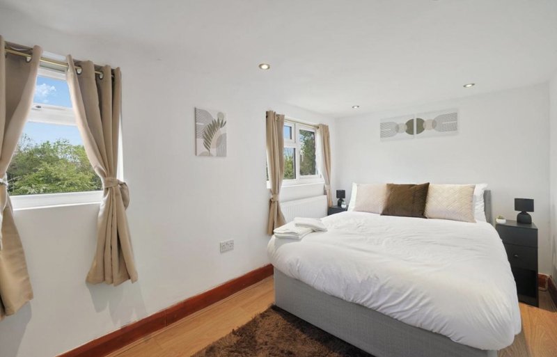 Bright modern bedroom with double bed, wooden flooring, large windows and neutral décor