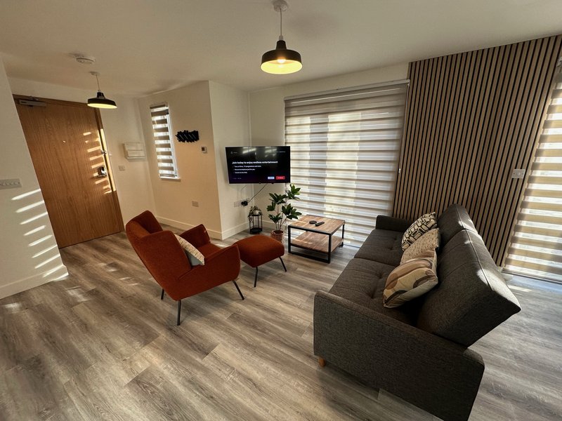Modern living room with grey sofa, red armchairs, wooden door, wall-mounted TV and pendant lighting
