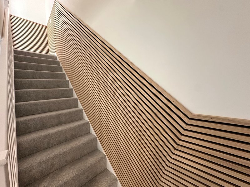Modern staircase with gray carpet and wooden slat handrail design
