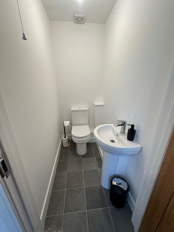 Compact bathroom with toilet, pedestal sink, gray tile floor and white walls