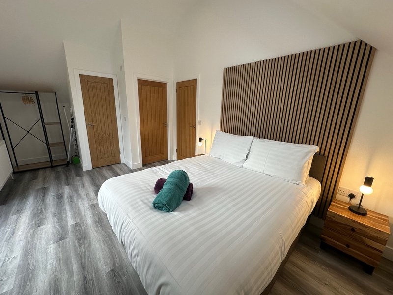Modern bedroom with large bed, green accent pillow, wooden doors and contemporary wall paneling