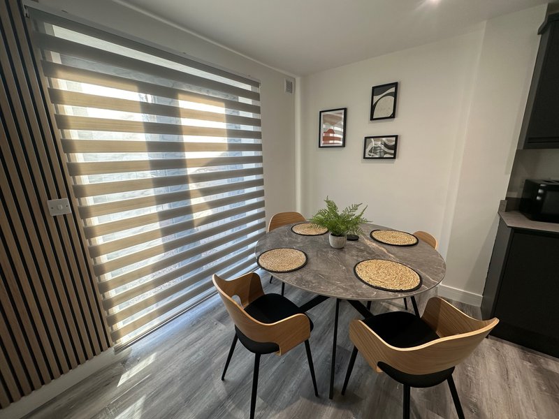 Modern dining area with round table, four chairs, striped blinds and wall art