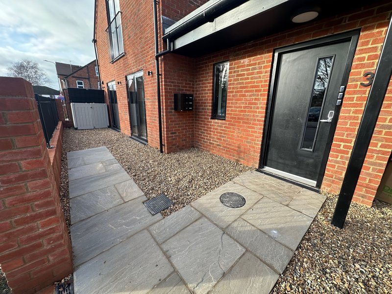 Modern brick building exterior with paved courtyard, gravel area, and black door entrance