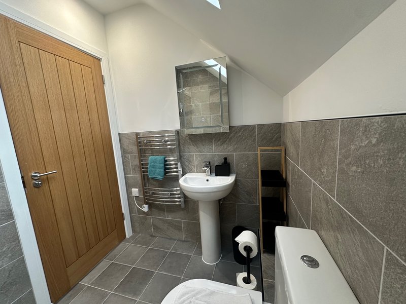 Modern bathroom with pedestal sink, mirror, toilet, and gray tile walls