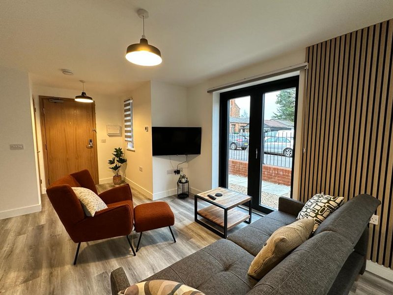 Modern living room with gray sofa, burgundy armchair, wall-mounted TV and glass doors to balcony