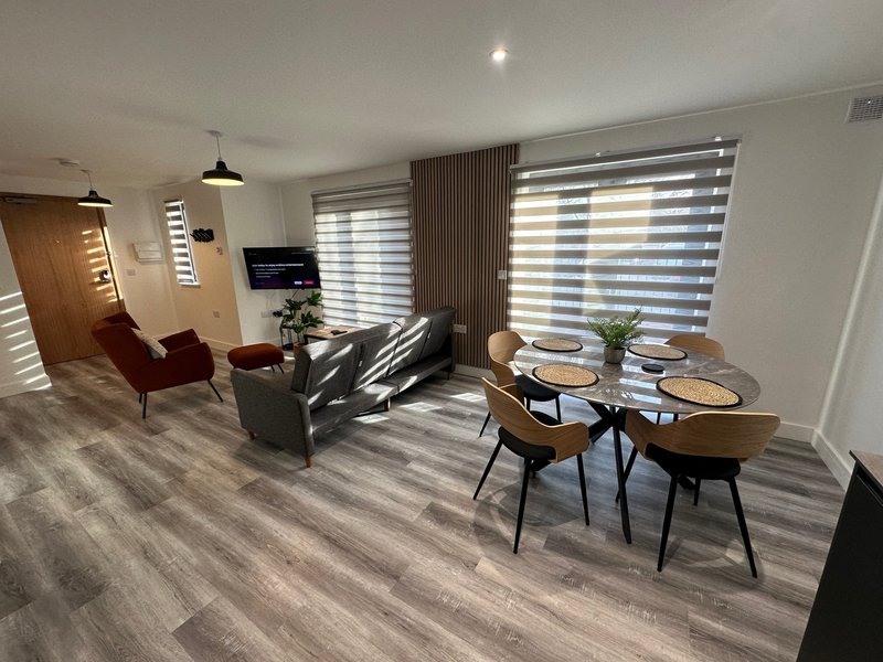 Modern open-plan living space with dining table, seating area, and kitchen visible through large windows