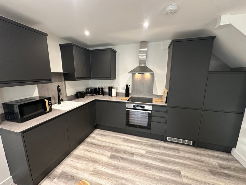 Modern kitchen with dark grey cabinets, white countertops, integrated appliances and wood-effect flooring