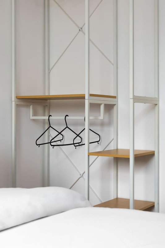 Modern bedroom wardrobe with white paneled doors, wooden shelves, and black hangers