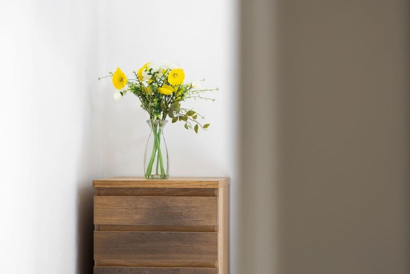 Wooden dresser with glass vase of yellow flowers and green foliage