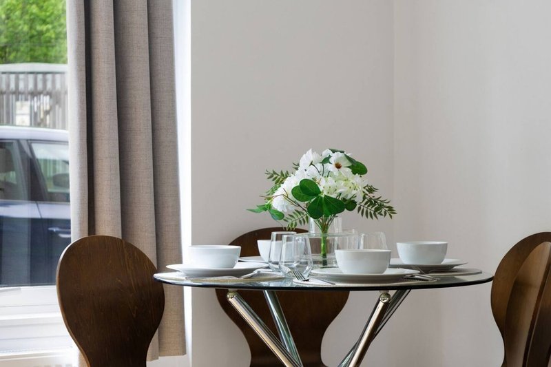 Dining area with round glass table, brown chairs, white flowers in vase, and garden view