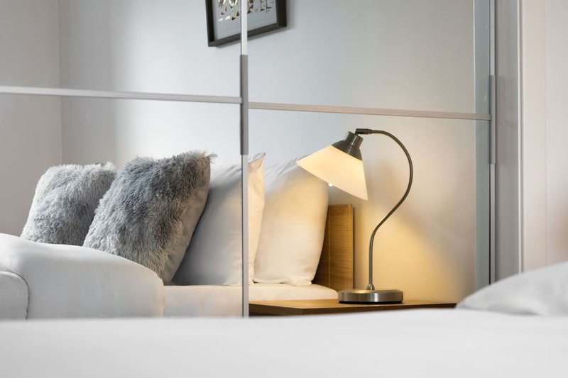 Bedroom bedside detail with lamp, pillows and decorative cushions on bed