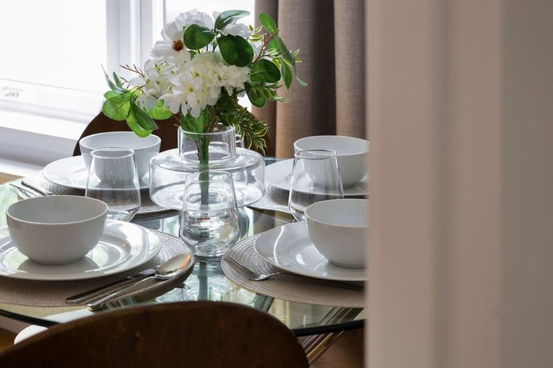 Dining table set with white place settings, water glasses, and fresh white flowers in vase