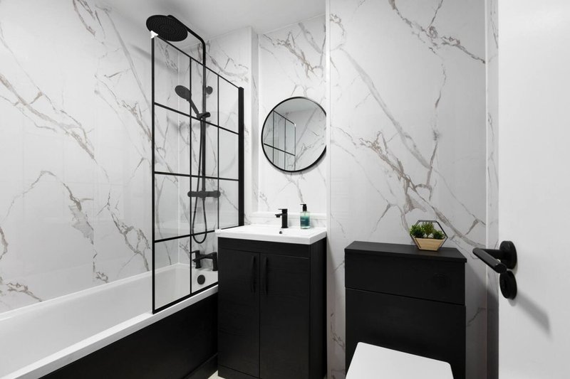 Modern bathroom with marble-effect tiles, black vanity, round mirror and glass shower enclosure