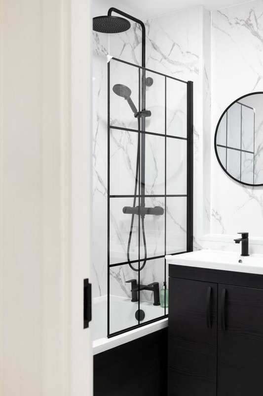 Modern bathroom with black and white shower enclosure, rainfall showerhead, black vanity and circular mirror