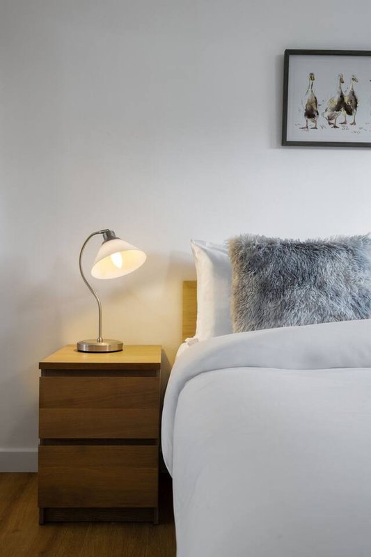 Bedroom with white bed, wooden nightstand, table lamp, and framed wall art