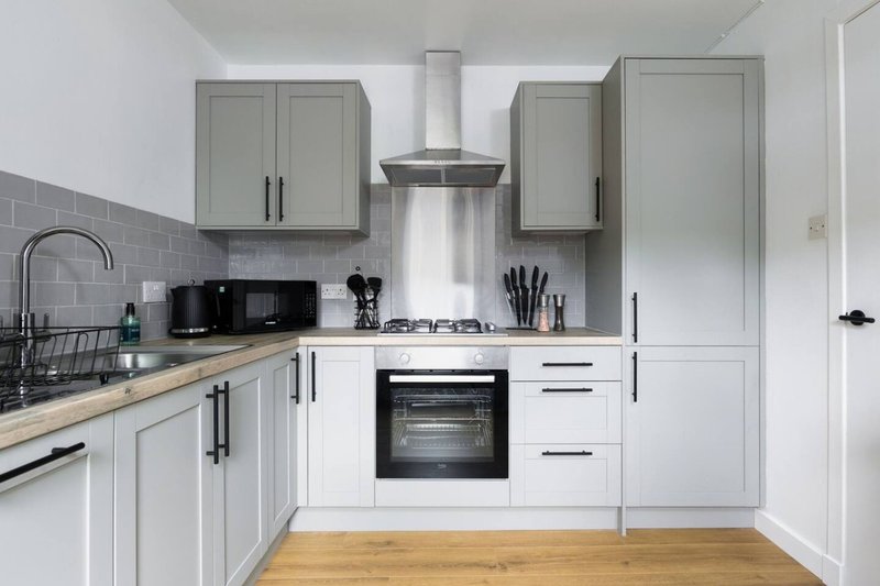 Modern kitchen with white cabinetry, grey tile splashback, stainless steel appliances and wooden flooring