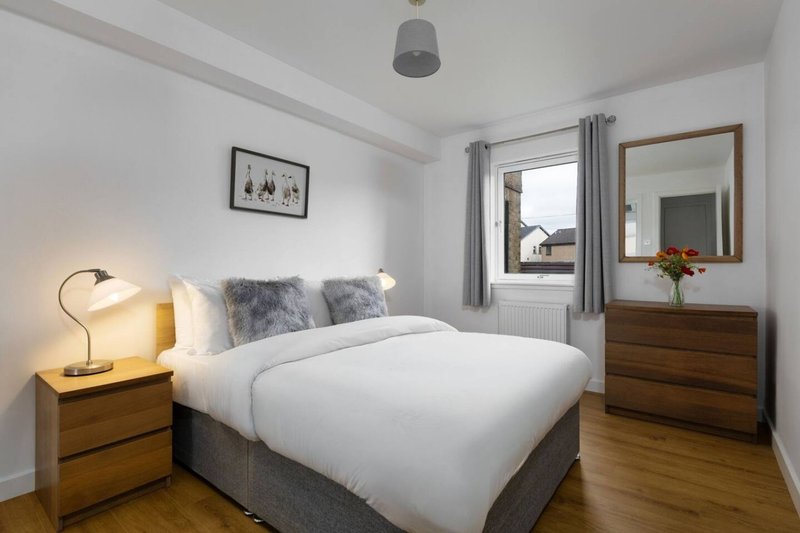 Bright bedroom with double bed, wooden furniture, grey cushions and pendant light