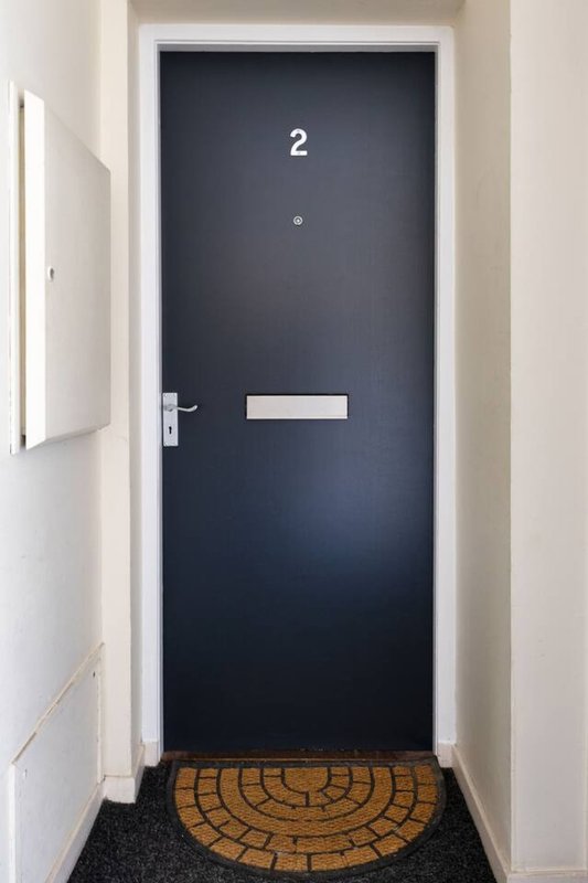 Dark blue apartment door numbered 2 with white handle and semi-circular doormat