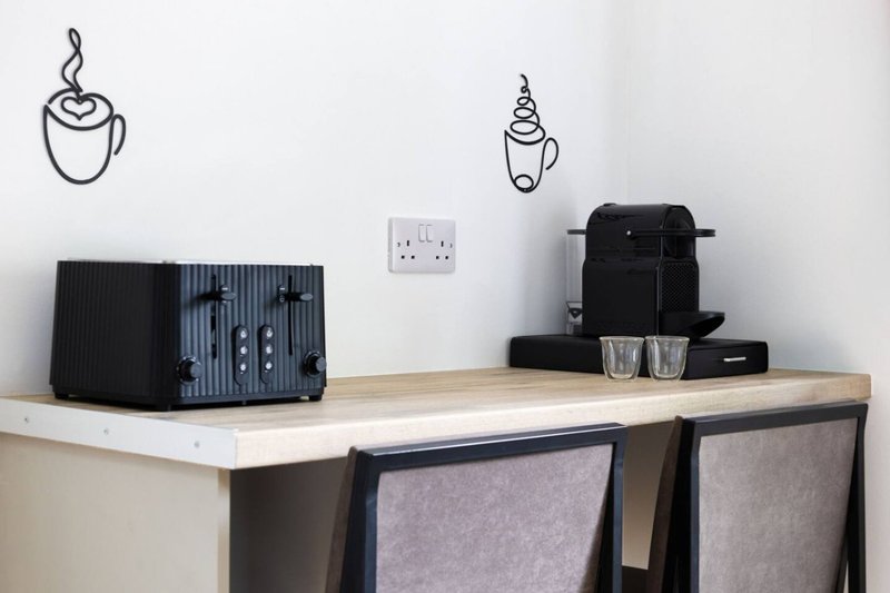Desk workspace with black kettle, toaster, wall-mounted coffee-themed line art decals, and electrical outlet