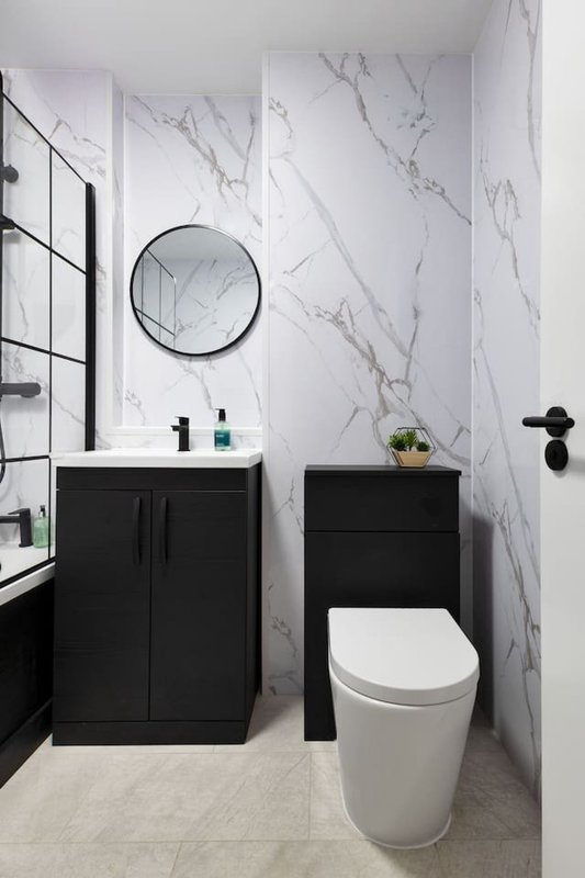 Modern bathroom with marble wall tiles, black vanity, round mirror, and white toilet