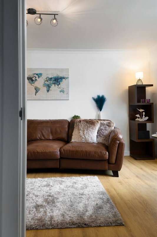 Living room with brown leather sofa, world map wall art, blue pampas grass, and wooden shelving unit