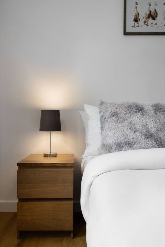 Modern bedroom with double bed, wooden nightstand, table lamp, and framed wall art