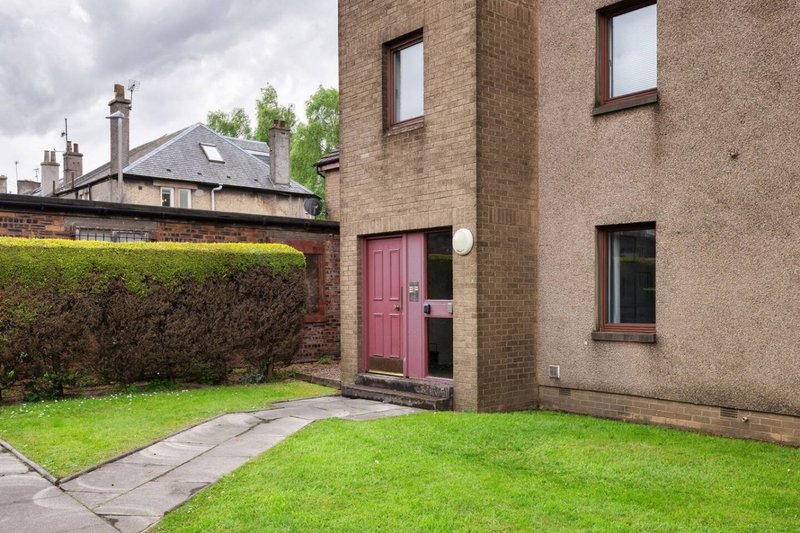 Brick house exterior with pink door, garden, paved pathway and adjacent properties