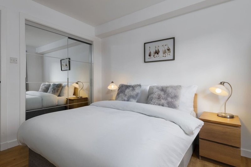 Modern bedroom with double bed, wooden nightstands, table lamps, and mirrored wardrobe