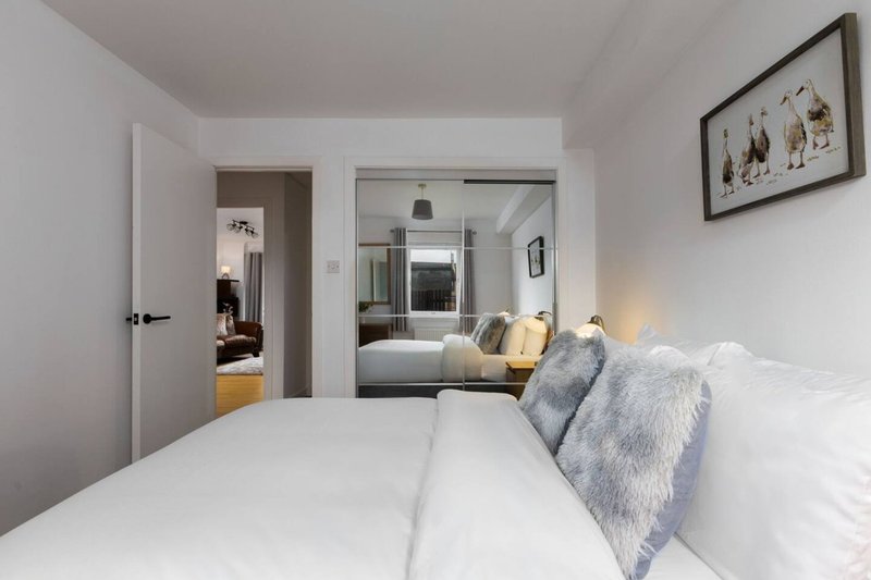 Modern bedroom with white bedding, grey fur throw pillows, and mirrored wardrobe doors