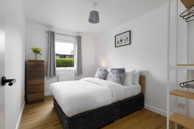 Bright bedroom with double bed, wooden nightstand, framed wall art, and garden view through window
