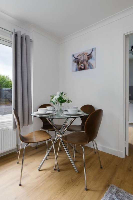 Dining area with round glass table, brown chairs, and artwork of Highland cattle on wall