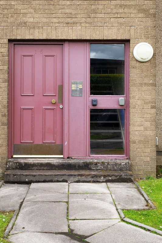 Brick building exterior with pink painted door and window, paved pathway and grass verge