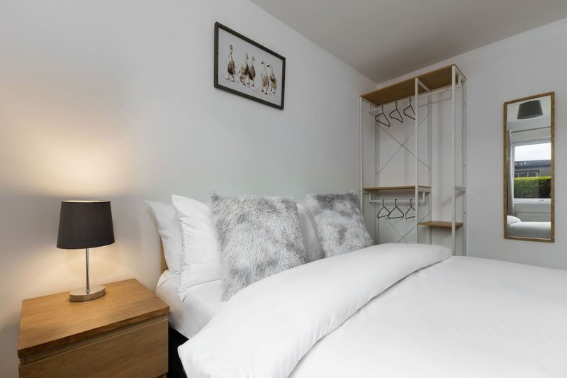 Bright bedroom with double bed, white bedding, grey cushions, wooden bedside table with lamp