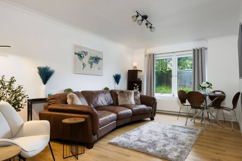 Bright living room with brown leather sofa, wooden floor, framed world map, and garden view