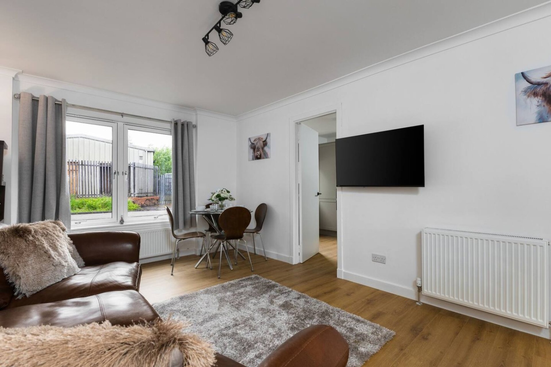 Bright living room with brown leather sofa, wooden floor, wall-mounted TV and glass doors to garden